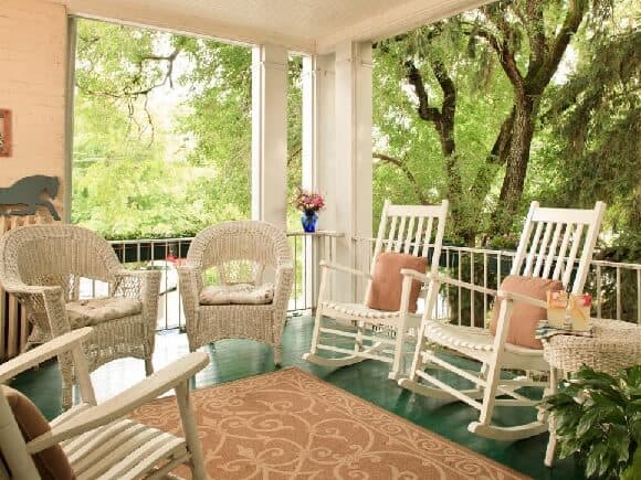 White wood rocking chairs and White Wicker accent chairs with pillows and Peach colored indoor outdoor rug with swirl design for front porch patio and pool