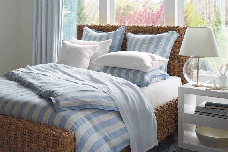 Casual Elegance Coastal Room Designs and Decor Ideas. Breezy Stripes bedroom collection by Serena and Lily. Blue and white stripes bedding, chunk woven wicker bed frame and headboard. White lacquer side table and clear glass table lamp with white lamp shade. (affiliate link) https://fave.co/2BfGokv