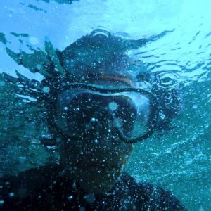 Adult in snorkle mask under blue water